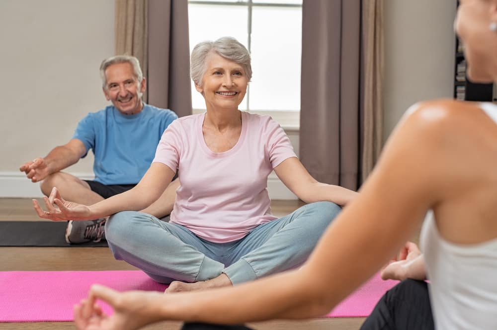 Smiling senior man and woman in yoga class, following young instructor