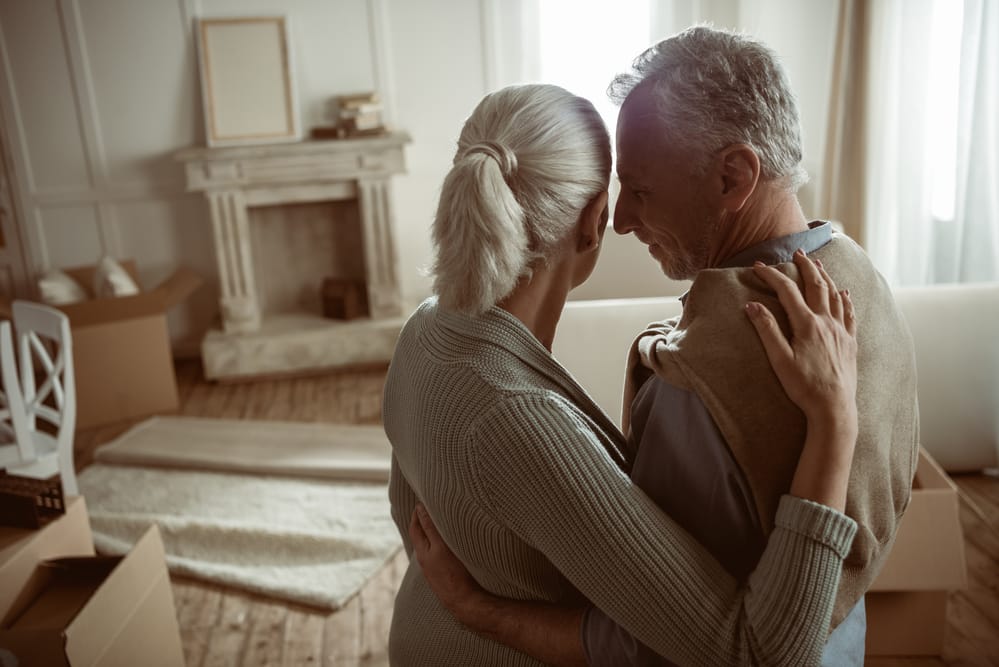Senior couple embracing, looking at room with packing boxes