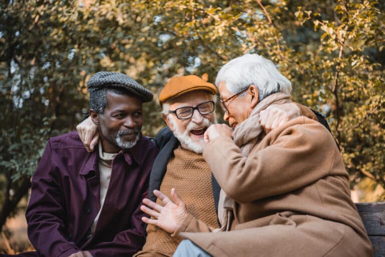 Three senior men laughing on a bench outside