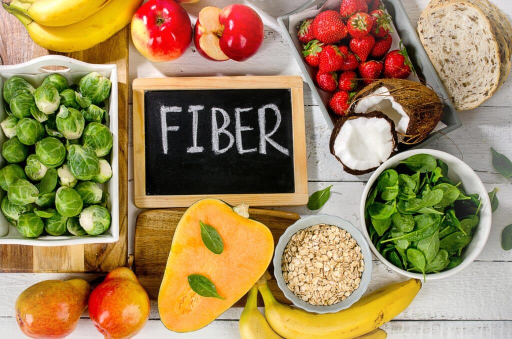 chalkboard sign reading fiber surrounded by vegetables, fruits, oats, etc