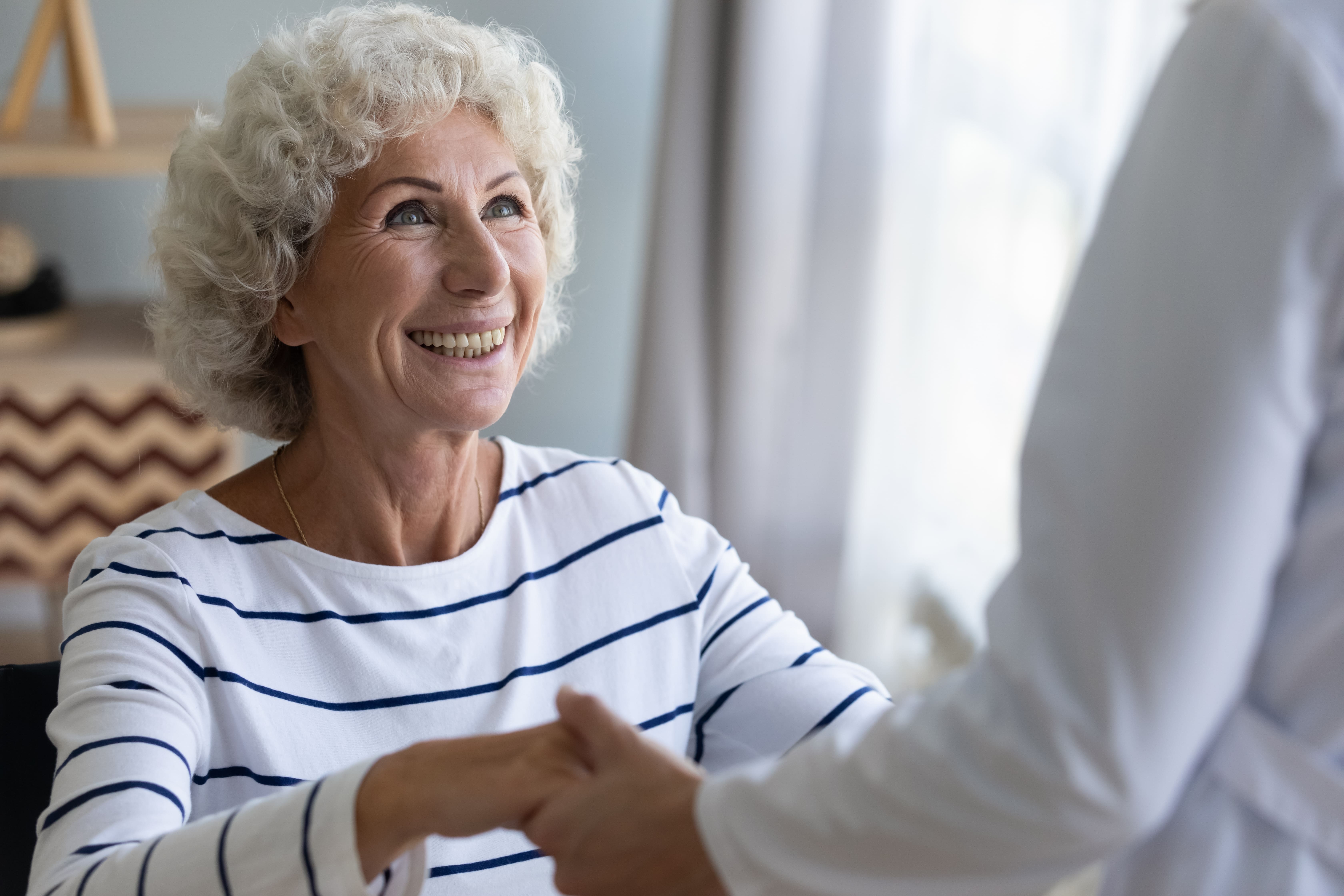 Smiling senior woman holding hands of someone out of frame